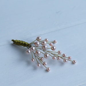 May include: A delicate, handmade brooch featuring a cluster of pale pink pearls on a green wire stem. The brooch is perfect for adding a touch of elegance to any outfit.