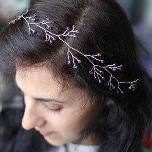 May include: A silver headband with a delicate vine design and purple beads. The headband is worn by a person with long dark hair.