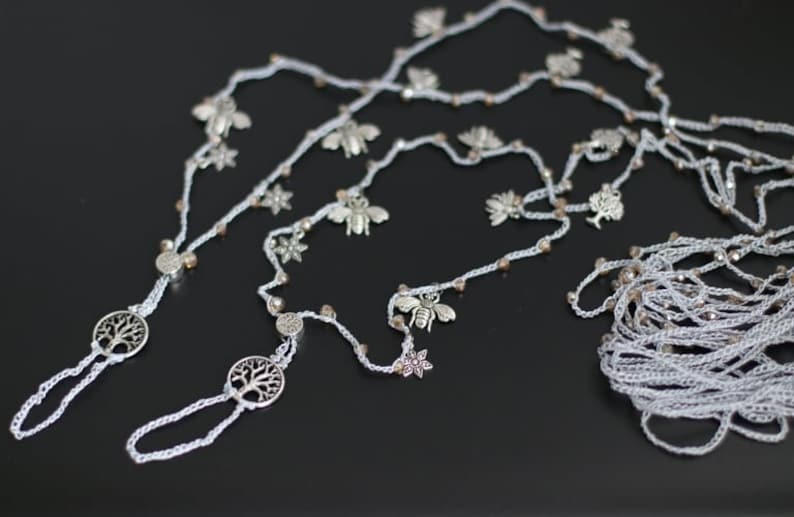 Puede incluir: Un par de joyas de pie de crochet blanco con dijes de &aacute;rbol de la vida plateados. Las joyas est&aacute;n enhebradas con cuentas y dijes plateados, incluyendo abejas, flores y hojas.