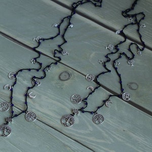 May include: A black beaded necklace with silver charms, including trees, moons, and stars. The necklace is laid out on a wooden surface.