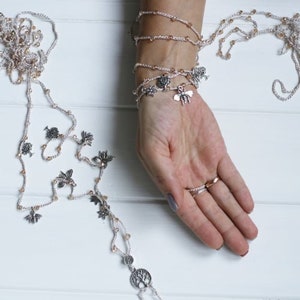 Puede incluir: Un delicado collar de cuentas de plata y oro con m&uacute;ltiples hilos y peque&ntilde;os amuletos, incluyendo p&aacute;jaros, abejas y un &aacute;rbol de la vida. El collar se coloca en capas en una mu&ntilde;eca, creando un efecto de pulsera.
