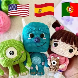 Puede incluir: Tres muñecos de ganchillo hechos a mano que incluyen un pequeño monstruo verde de un ojo, un monstruo azul más grande con cuernos y una figura humana con pelo castaño en coletas, vistiendo una camisa rosa y sosteniendo una criatura marrón.
