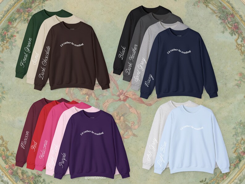 May include: A collection of crewneck sweatshirts in various colors including forest green, sand, dark chocolate, black, dark heather, sport grey, navy, maroon, red, heliconia, light pink, purple, ash grey, and light blue, each with the text I'd rather be reading.
