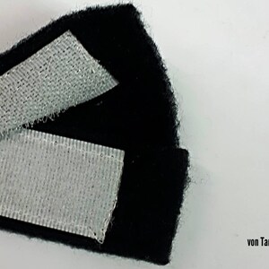 May include: Close-up of black fabric with two strips of white hook and loop fastener. The fabric is folded over to show the fastener.
