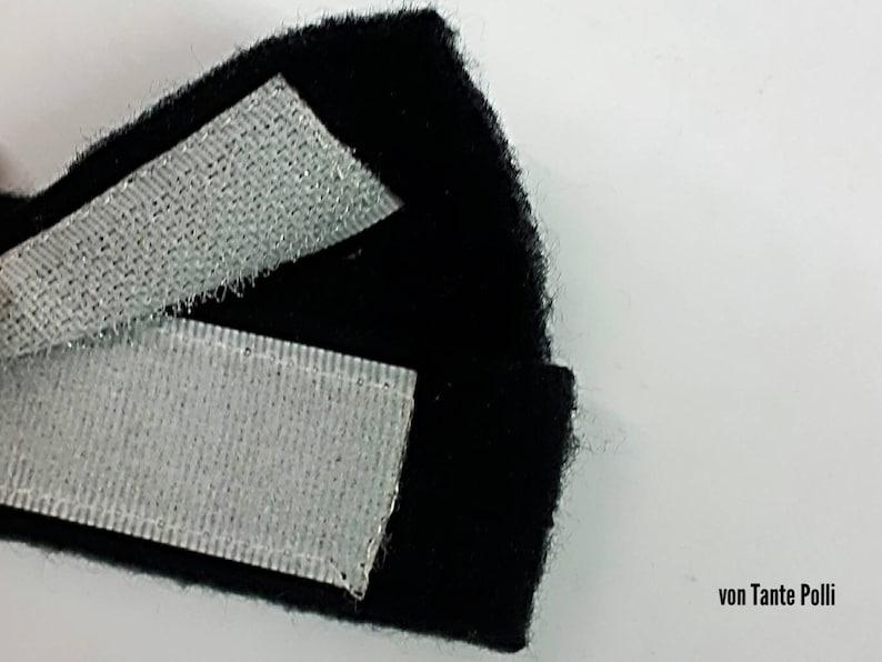 May include: Close-up of black fabric with two strips of white hook and loop fastener. The fabric is folded over to show the fastener.