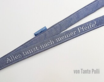 May include: A blue denim ribbon with white embroidery that reads "Alles tanzt nach meiner Pfeife! von Tante Polli".