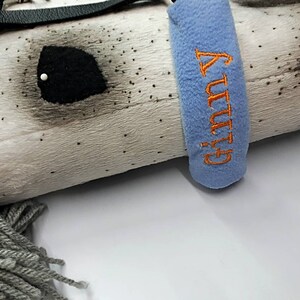 May include: A white and gray plush horse head with a black leather strap and a blue fleece collar with the word "GUTSY" embroidered in orange.