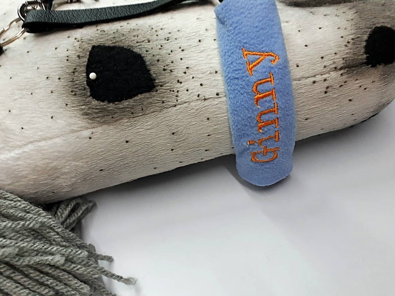 May include: A white and gray plush horse head with a black leather strap and a blue fleece collar with the word "GUTSY" embroidered in orange.