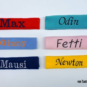 May include: Six personalized fabric labels with different names embroidered on them. The labels are in various colors, including red, blue, yellow, pink, and turquoise. The text on the labels reads: Max, Odin, Ginny, Fetti, Mausi, and Newton. The labels are all from "von Tante Polli."