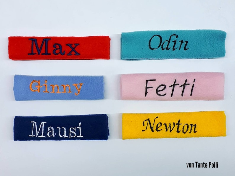 May include: Six personalized fabric labels with different names embroidered on them. The labels are in various colors, including red, blue, yellow, pink, and turquoise. The text on the labels reads: Max, Odin, Ginny, Fetti, Mausi, and Newton. The labels are all from "von Tante Polli."
