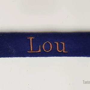 May include: A navy blue fabric label with the name "Lou" embroidered in orange thread.