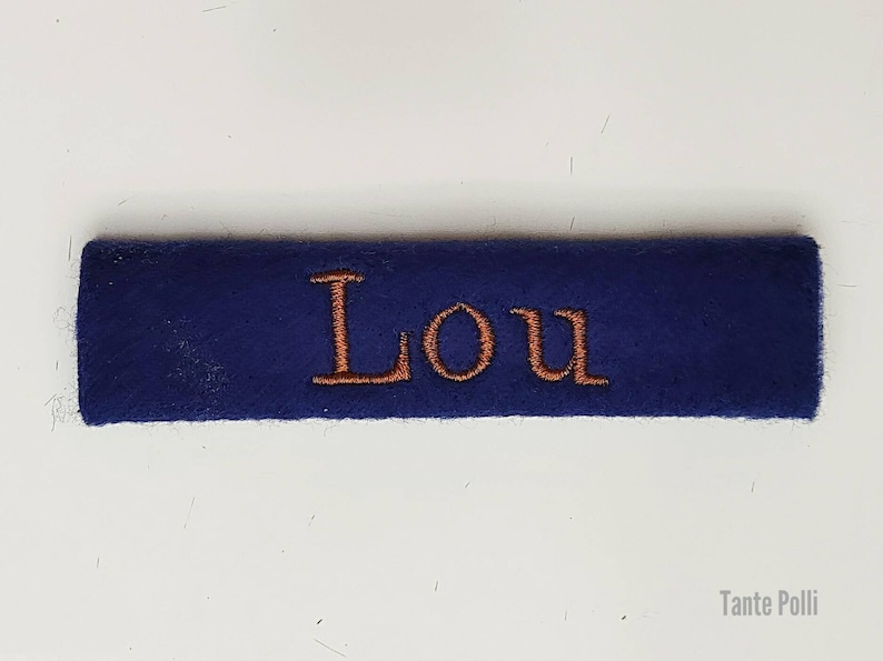 May include: A navy blue fabric label with the name "Lou" embroidered in orange thread.