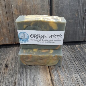 Puede incluir: Dos barras de jab&oacute;n de leche de cabra hecho a mano con un patr&oacute;n de remolino verde, amarillo y blanco. El jab&oacute;n est&aacute; etiquetado como "ORAGE d'&Eacute;T&Eacute;" y "Savon au lait de ch&egrave;vre fait &agrave; la Main - Handmade Goat Milk Soap -."