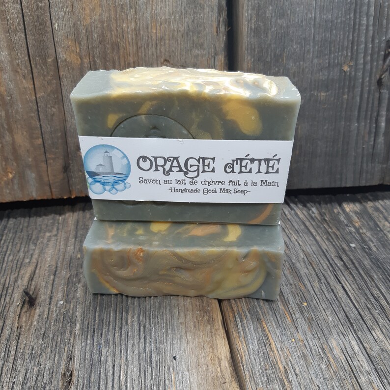 Puede incluir: Dos barras de jab&oacute;n de leche de cabra hecho a mano con un patr&oacute;n de remolino verde, amarillo y blanco. El jab&oacute;n est&aacute; etiquetado como "ORAGE d'&Eacute;T&Eacute;" y "Savon au lait de ch&egrave;vre fait &agrave; la Main - Handmade Goat Milk Soap -."