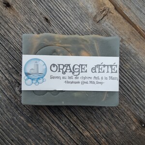 Puede incluir: Una pastilla de jab&oacute;n de leche de cabra hecho a mano con una etiqueta que dice "ORAGE C'&Eacute;T&Eacute; Savon au lait de ch&egrave;vre fait &agrave; la Main -Handmade Goat Milk Soap-". El jab&oacute;n es de color verde oscuro con remolinos de naranja y marr&oacute;n.