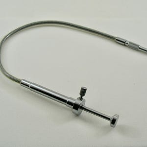 Peut inclure: Un outil de ramassage à griffe flexible de couleur argentée. Il comprend une tige métallique enroulée et un mécanisme de préhension. L'outil possède un petit bouton pour le contrôle et une pointe filetée. Conçu pour récupérer de petits objets.