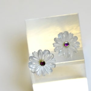 Könnte beinhalten: Ein Paar weiße, blumenförmige Ohrringe mit einem kleinen rosafarbenen Edelstein in der Mitte jeder Blume.