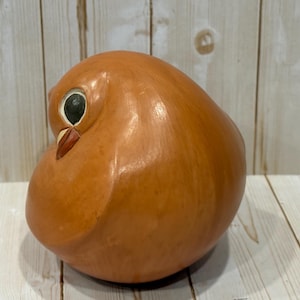 May include: A handcrafted, brown owl figurine with a rounded body and a detailed face. The owl has a black eye, a red beak, and is made of a smooth, polished material. The owl is a decorative item.