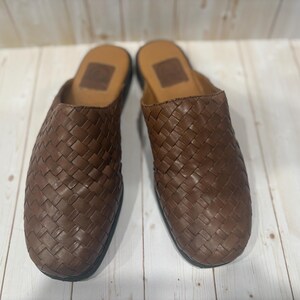 May include: A pair of brown leather woven slip-on shoes. The shoes have a dark brown woven pattern on the top and a brown leather insole. The soles are black.