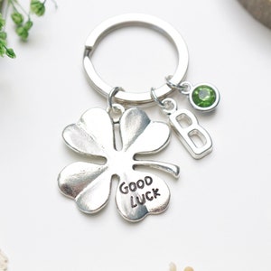 以下が含まれることがあります： 緑色の宝石、文字「B」のチャーム、そしてクローバーに刻まれた「幸運を祈って」という文字が付いた、銀製の四つ葉のクローバーキーホルダー。