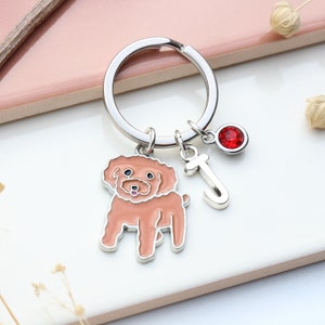 May include: A silver key chain with a red rhinestone charm, a silver letter J charm, and a charm of a brown poodle.
