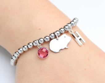 Puede incluir: Una pulsera elástica de cuentas metálicas plateadas con tres dijes colgantes: un cristal rosa facetado redondo, una silueta plana de cobaya en tono plateado y un dije con la letra H en bloque de tono plateado.