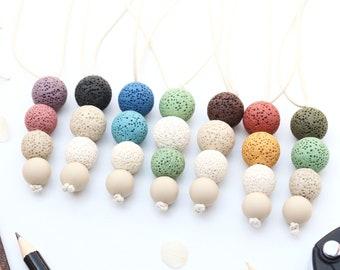 May include: A set of seven lava stone bead necklaces, each with three beads in different colors, including beige, brown, green, blue, purple, and orange. The necklaces are strung on a natural white cord.