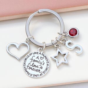 Könnte beinhalten: Silberner Schlüsselanhänger mit einem Herz, einem Stern, einem Buchstaben S-Anhänger und einem runden Anhänger mit dem Text "A family's love is forever" und einem kleinen Herzen.