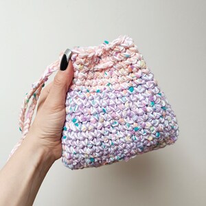 May include: A small, crocheted drawstring bag with a pink, purple, and turquoise color gradient. The bag is made with a textured, speckled yarn.