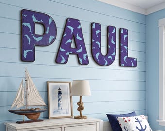 May include: Large wall-mounted letters spelling the name PAUL, featuring a dark purple background with a repeating pattern of light blue dolphins. Each letter has a dark border and a stitched-look edge, creating a decorative display.