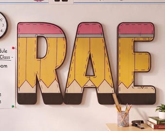 May include: Three large wooden wall letters spelling RAE, designed to look like yellow pencils with pink erasers and black graphite tips. The letters feature a wood grain texture and dark outlines, mounted on a wall above a desk with school supplies.