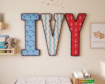 May include: Three large wall-mounted letters spelling IVY. The letter I features a light blue background with dark blue scalloped patterns. The letter V has light blue wavy vertical stripes. The letter Y is red with a white anchor pattern.