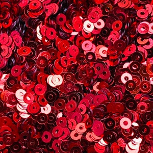 May include: A close-up image of a large quantity of red metallic sequins. The sequins are arranged in a random pattern and are all the same size and shape.