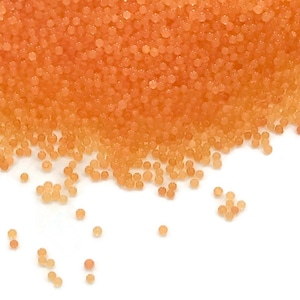 May include: A close-up of a pile of small, round, orange beads. The beads are scattered on a white surface.