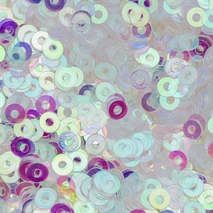 May include: A close-up of iridescent sequins in a variety of shades of white and purple. The sequins are arranged in a random pattern and are all the same size and shape.