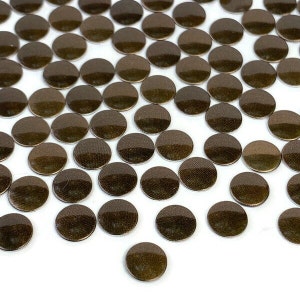 May include: A large quantity of small, round, metallic gold-colored embellishments. The embellishments are scattered on a white surface.