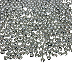 May include: A collection of small, faceted, gray rhinestones scattered across a white surface. Each rhinestone has a multi-faceted surface, reflecting light. The rhinestones are round with a flat back, suitable for various craft projects.