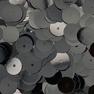 May include: A pile of black round sequins with a hole in the center. The sequins have a textured surface.