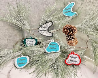 Może przedstawiać: Sześć świątecznych ozdób w kształcie nowoczesnych bumerangów z połowy XX wieku z napisem "Happy Holidays" na każdej. Ozdoby są w różnych kolorach, w tym turkusowym, niebieskozielonym, czerwonym i białym.