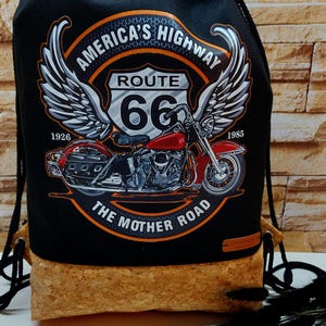 Peut inclure: Sac à cordon noir avec un fond en liège. Le sac présente un motif de moto avec des ailes et un panneau Route 66. Le texte "America's Highway" et "The Mother Road" est imprimé sur le sac.