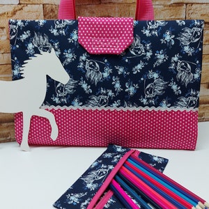 Könnte beinhalten: Eine rosa-blaue Stoff-Stiftetui mit Reißverschluss und einem weißen Pferde-Design. Die Etui ist mit Buntstiften gefüllt.