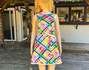 May include: A sleeveless, colorful dress with a geometric pattern. The dress features a vibrant mix of pink, yellow, green, and blue squares, outlined with navy blue lines. The dress has a white trim and is displayed on a mannequin.