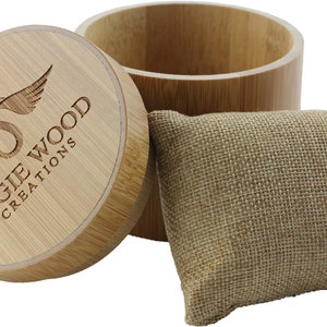 May include: A round wooden box with a lid. The lid has a logo that says "Angie Wood Creations" with a stylized bird design. The box is sitting on a white background next to a small burlap pouch.