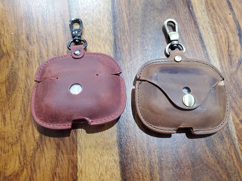 May include: Two leather cases with keychains for wireless earbuds. The case on the left is red and the case on the right is brown.