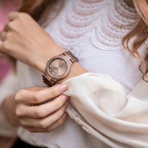 May include: A brown wooden wristwatch with a silver face and a white background. The watch has a brown leather band.