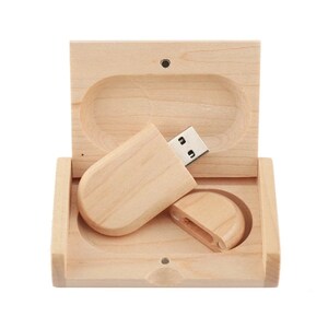 K&ouml;nnte beinhalten: Ein USB-Stick aus Holz in einer Holzkiste. Der Stick ist oval geformt und hat einen silbernen USB-Stecker. Die Kiste ist aus hellem Holz und hat einen Klappdeckel.