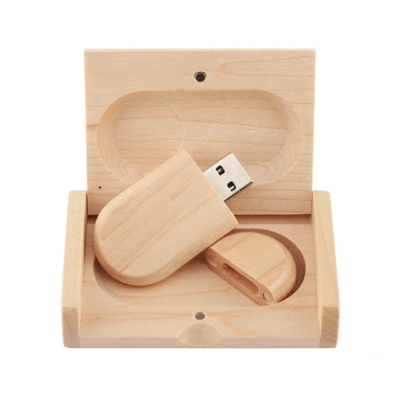 K&ouml;nnte beinhalten: Ein USB-Stick aus Holz in einer Holzkiste. Der Stick ist oval geformt und hat einen silbernen USB-Stecker. Die Kiste ist aus hellem Holz und hat einen Klappdeckel.
