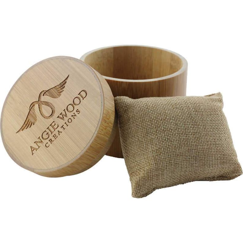 May include: A wooden box with a lid that has the logo "Angie Wood Creations" with a winged infinity symbol. The box is open and a small brown burlap pouch is sitting next to it.