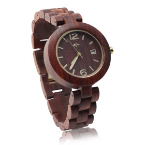 May include: A dark red wooden wristwatch with a round face and gold-colored hands and hour markers. The watch has a wooden band.