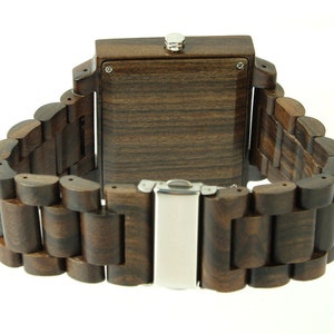 May include: A dark brown wooden wristwatch with a square face and a metal clasp. The watch band is made of linked wooden pieces.